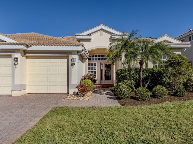 view of front of house with decorative driveway, a tile roof, stucco siding, a front yard, and a garage