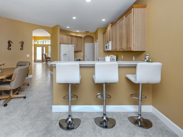 kitchen with white appliances, arched walkways, a breakfast bar, a peninsula, and light countertops