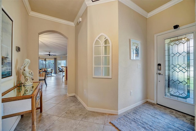 foyer entrance with arched walkways, crown molding, light tile patterned floors, a ceiling fan, and baseboards