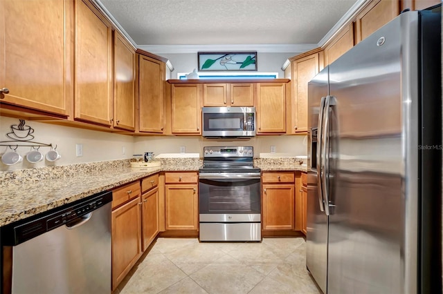 kitchen featuring a textured ceiling, light tile patterned floors, light stone countertops, stainless steel appliances, and brown cabinets