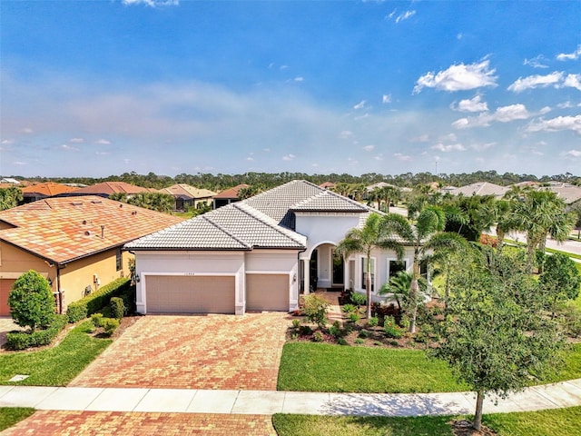 mediterranean / spanish house featuring decorative driveway, a tiled roof, an attached garage, and stucco siding