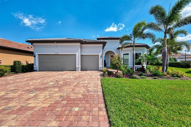 mediterranean / spanish home with stucco siding, a tile roof, an attached garage, decorative driveway, and a front yard