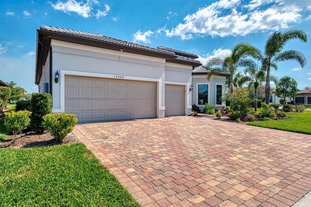 mediterranean / spanish house featuring a garage, a tile roof, decorative driveway, and stucco siding