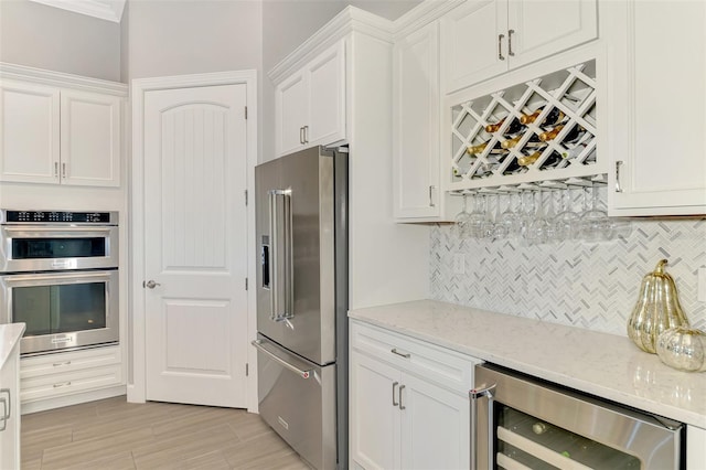 kitchen with beverage cooler, appliances with stainless steel finishes, light stone countertops, and white cabinets