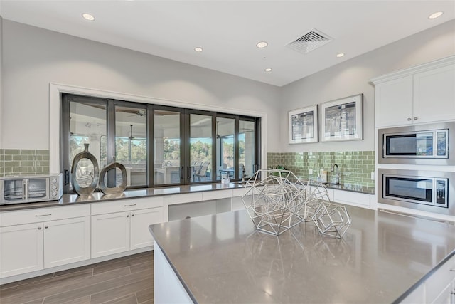 kitchen featuring white cabinetry, visible vents, stainless steel microwave, and decorative backsplash