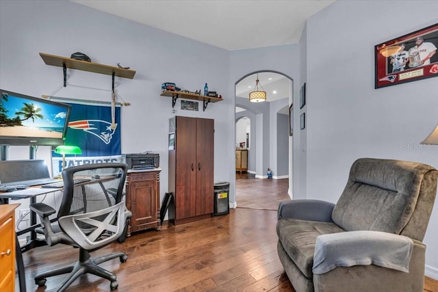 office area with arched walkways, wood finished floors, and baseboards