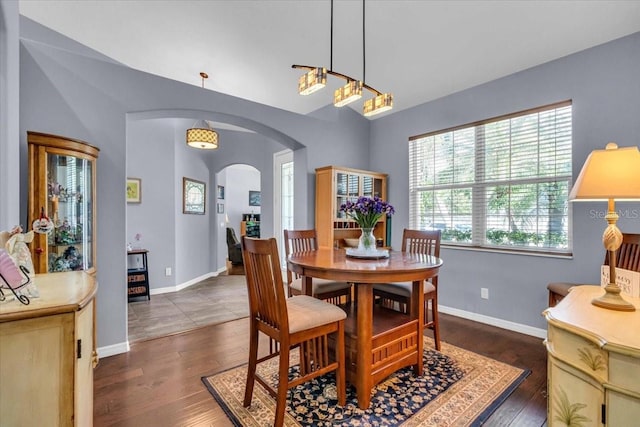 dining area featuring arched walkways, vaulted ceiling, baseboards, and wood finished floors