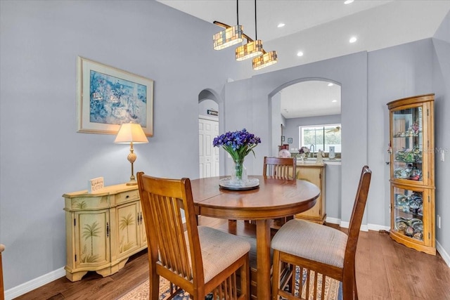 dining space with arched walkways, recessed lighting, baseboards, and wood finished floors