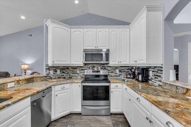 kitchen featuring decorative backsplash, white cabinets, lofted ceiling, light stone counters, and stainless steel appliances