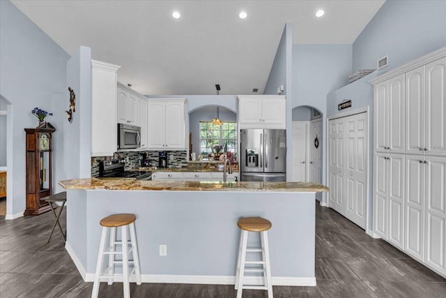 kitchen with appliances with stainless steel finishes, arched walkways, a peninsula, and a kitchen bar