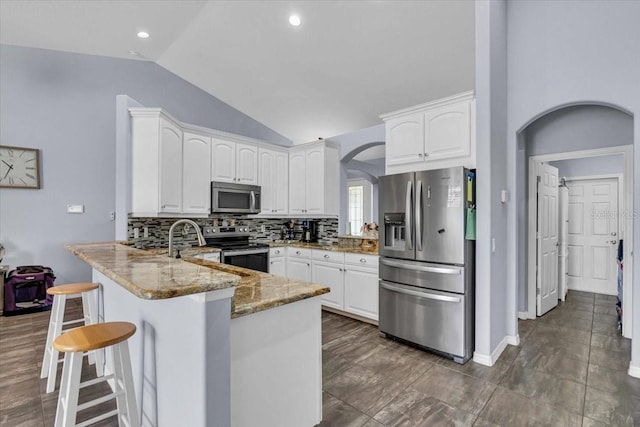 kitchen featuring arched walkways, light stone counters, stainless steel appliances, a peninsula, and tasteful backsplash