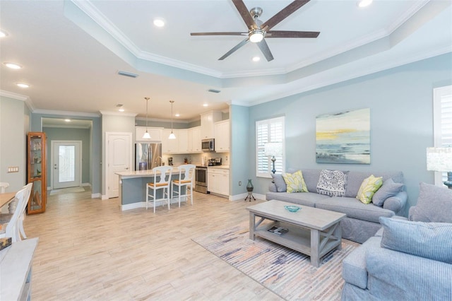 living room featuring light wood-style flooring, visible vents, baseboards, a raised ceiling, and crown molding