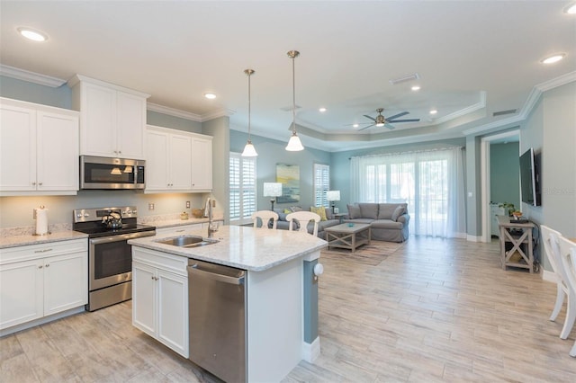 kitchen featuring appliances with stainless steel finishes, open floor plan, light wood-type flooring, white cabinetry, and a sink