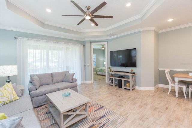 living room with light wood-type flooring, a raised ceiling, crown molding, and baseboards