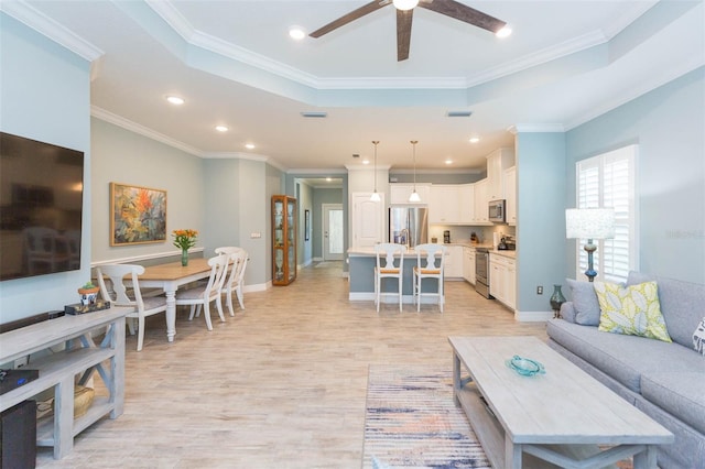 living area with baseboards, light wood finished floors, a raised ceiling, and crown molding