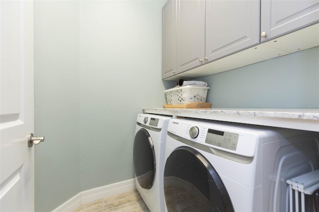 laundry room featuring light wood-style floors, washing machine and clothes dryer, cabinet space, and baseboards