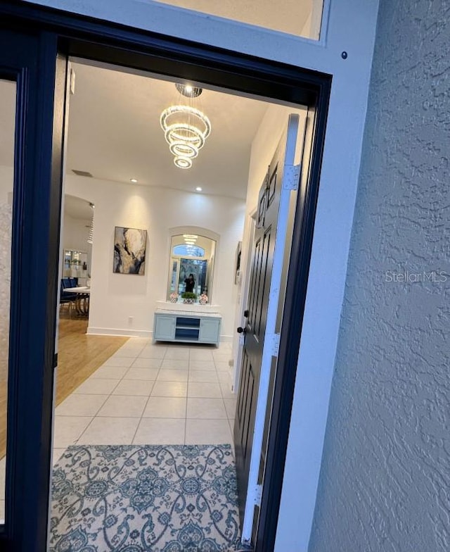 hallway with a chandelier, light tile patterned flooring, and baseboards