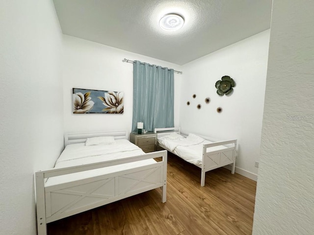 bedroom with a textured ceiling, wood finished floors, and baseboards