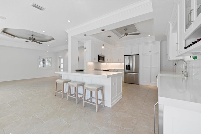 kitchen with ornamental molding, a sink, appliances with stainless steel finishes, a breakfast bar area, and a raised ceiling