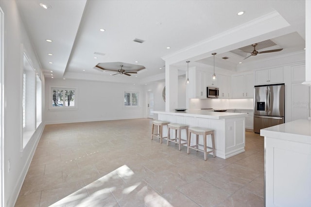 kitchen with appliances with stainless steel finishes, a raised ceiling, a kitchen breakfast bar, and ornamental molding