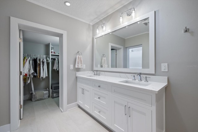 bathroom with a textured ceiling, double vanity, ornamental molding, and a sink