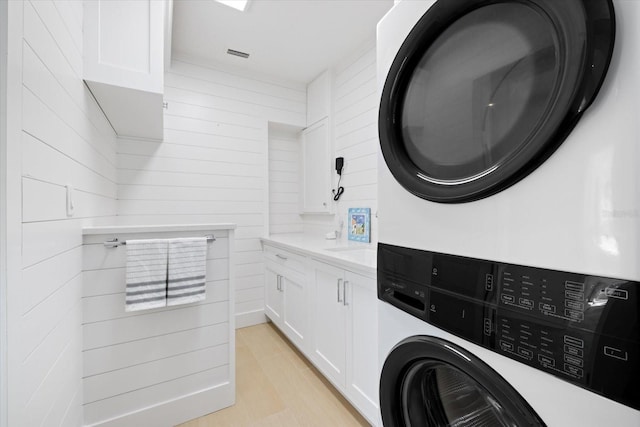 washroom with stacked washer / drying machine, cabinet space, and light wood finished floors