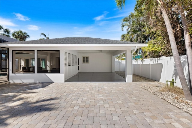 exterior space with decorative driveway, a shingled roof, fence, a sunroom, and a carport