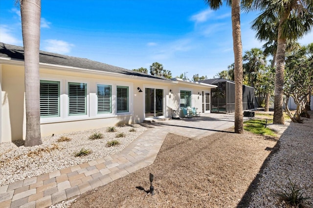 rear view of house with a lanai, a patio area, stucco siding, and a shingled roof