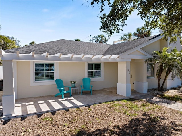 rear view of house featuring stucco siding, a shingled roof, and a patio area