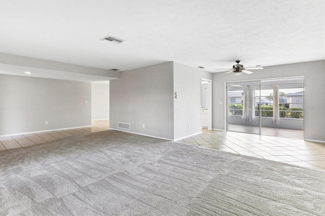 carpeted spare room with tile patterned flooring, a ceiling fan, visible vents, and baseboards