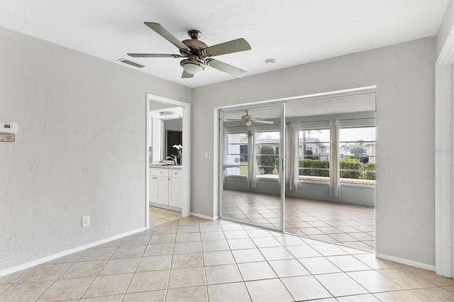 spare room with visible vents, baseboards, light tile patterned floors, a textured wall, and a ceiling fan