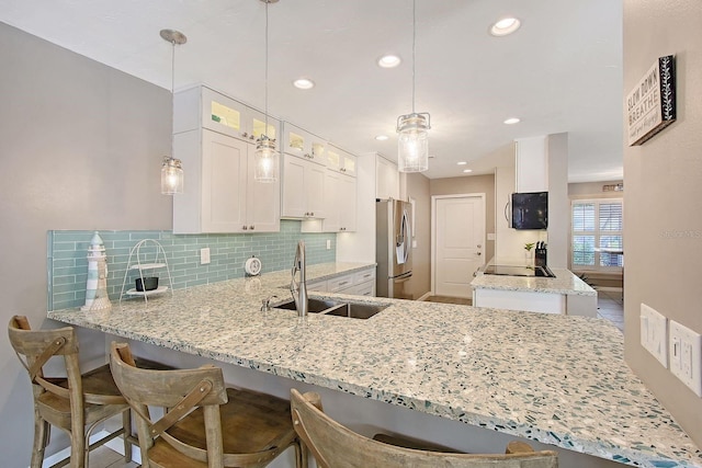 kitchen featuring light stone counters, a peninsula, a sink, stainless steel fridge with ice dispenser, and decorative backsplash