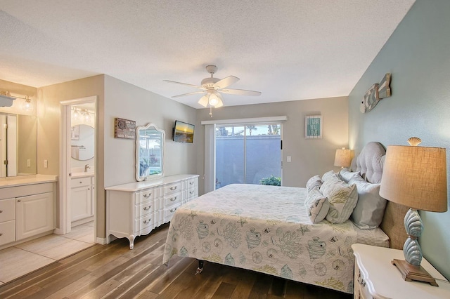 bedroom with light wood-style floors, a textured ceiling, ensuite bath, and a ceiling fan