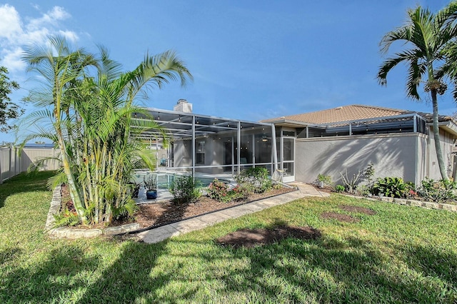 back of property featuring glass enclosure, a fenced backyard, a tiled roof, a lawn, and an outdoor pool