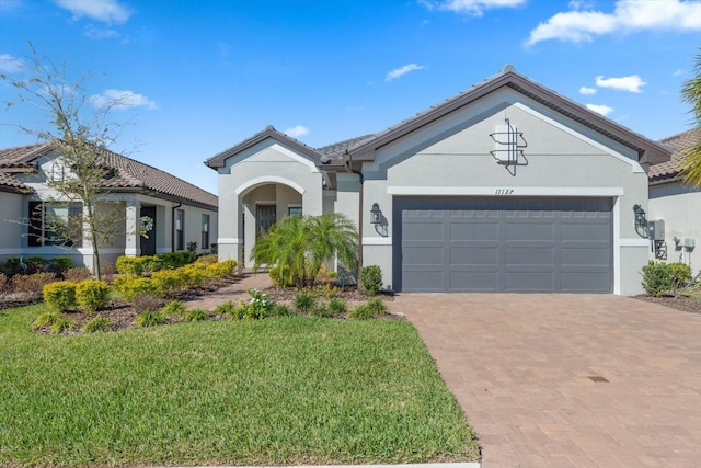 ranch-style house featuring decorative driveway, stucco siding, a front yard, a garage, and a tiled roof