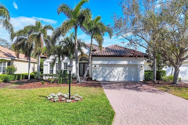 mediterranean / spanish home featuring decorative driveway, a tile roof, stucco siding, an attached garage, and a front lawn