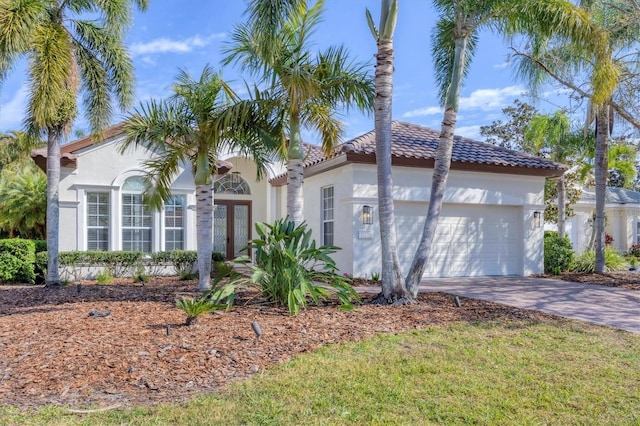 mediterranean / spanish house with a garage, driveway, a tiled roof, and stucco siding