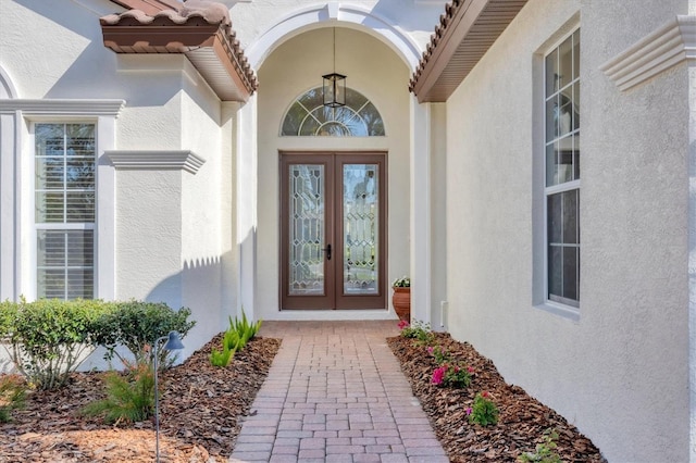 view of exterior entry with french doors, a tiled roof, and stucco siding