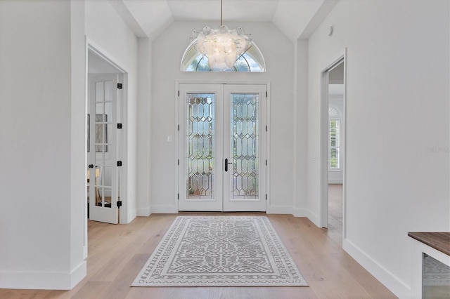 foyer entrance featuring light wood-type flooring, baseboards, lofted ceiling, and french doors