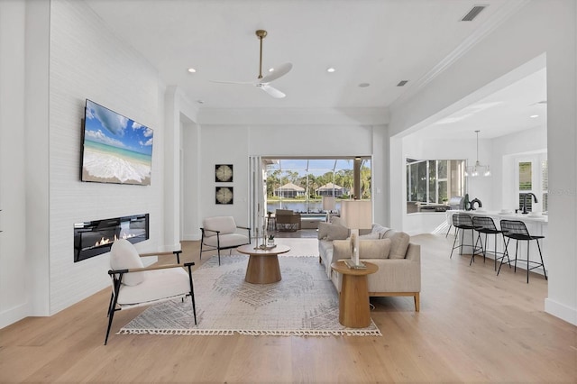 living room featuring light wood-style floors, a glass covered fireplace, visible vents, and ornamental molding