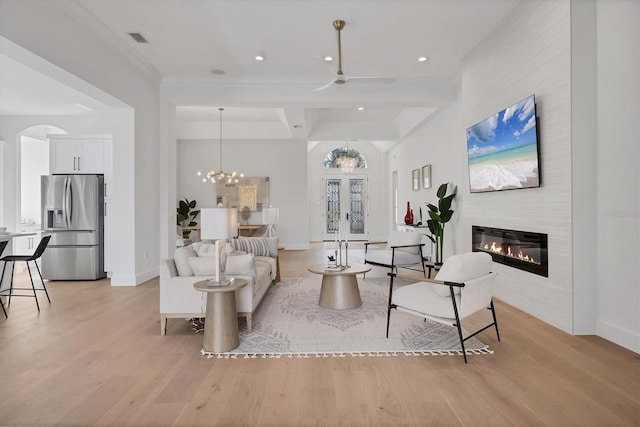 living area featuring visible vents, arched walkways, baseboards, a glass covered fireplace, and light wood-style flooring