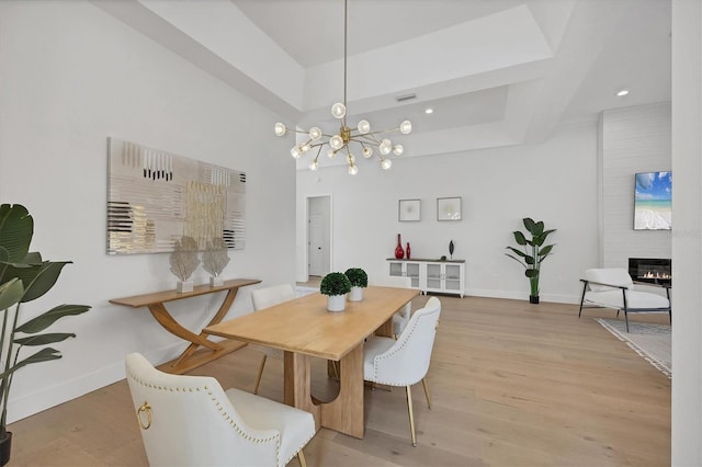 dining area with light wood-style floors, a chandelier, a fireplace, and baseboards