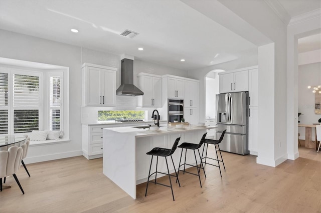 kitchen featuring appliances with stainless steel finishes, wall chimney range hood, a breakfast bar area, and light wood finished floors