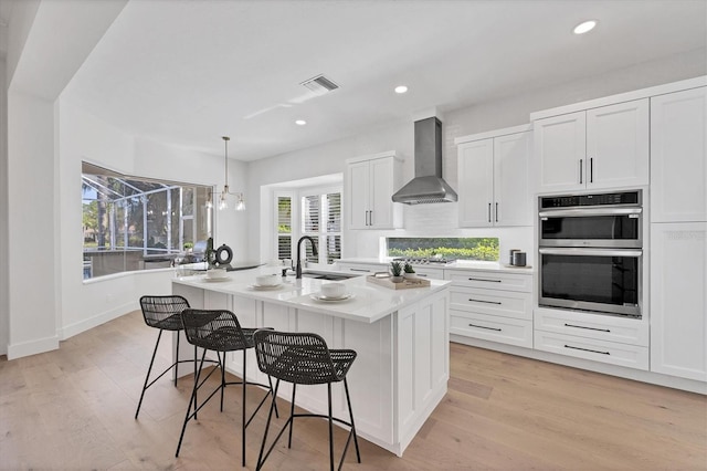 kitchen with a kitchen island with sink, stainless steel appliances, a sink, visible vents, and wall chimney exhaust hood