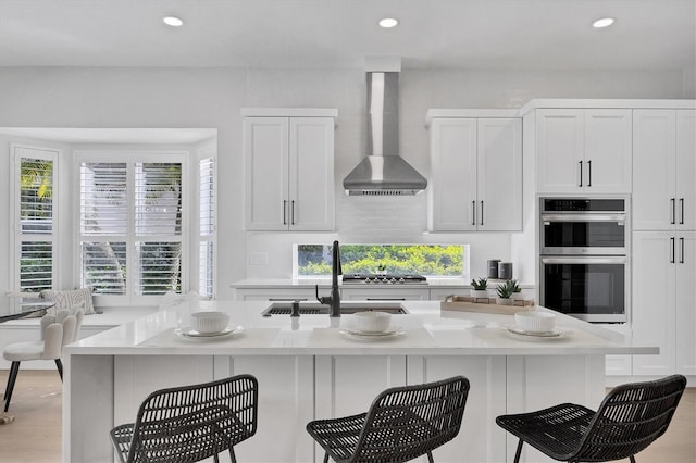 kitchen featuring wall chimney exhaust hood, appliances with stainless steel finishes, light countertops, and white cabinets