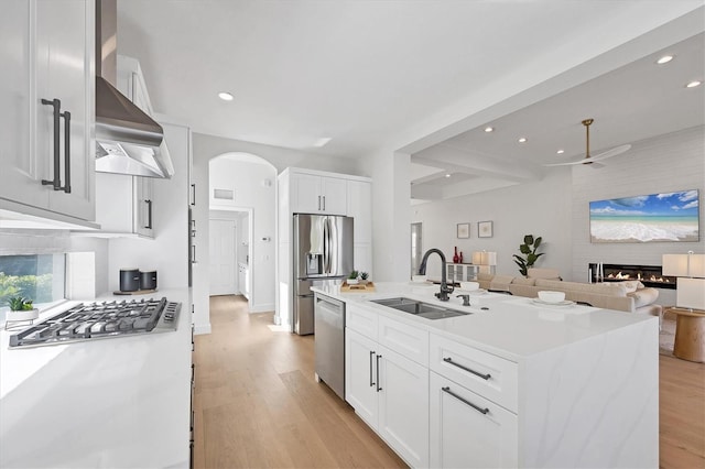 kitchen featuring arched walkways, a glass covered fireplace, light wood-style flooring, appliances with stainless steel finishes, and a sink