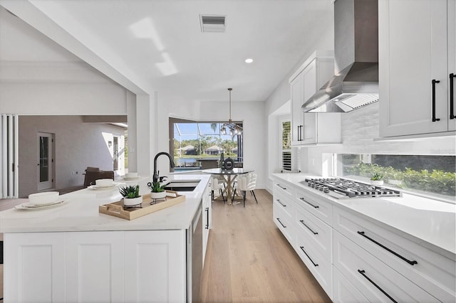 kitchen with tasteful backsplash, wall chimney exhaust hood, light wood-style flooring, stainless steel gas stovetop, and a sink