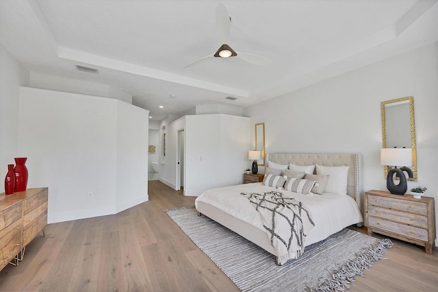 bedroom featuring a raised ceiling, visible vents, ensuite bathroom, wood finished floors, and baseboards