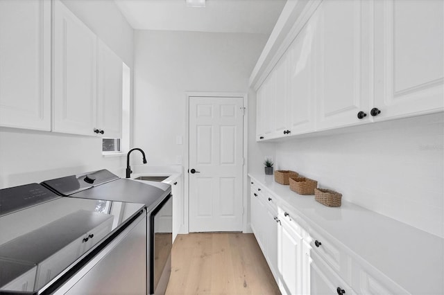 washroom with cabinet space, a sink, washer and clothes dryer, and light wood finished floors