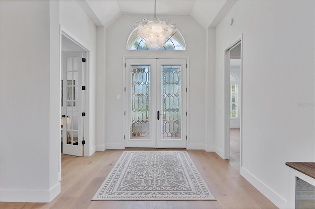 entryway featuring french doors, a chandelier, light wood-type flooring, vaulted ceiling, and baseboards